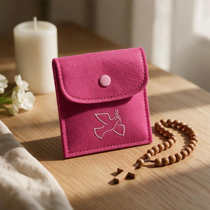 Rosenkranztasche aus pinkem Filz mit Taube auf Holztisch, daneben Holz-Rosenkranz, Kerze und weiße Blumen