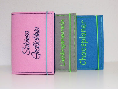 Drei personalisierte Kalenderhüllen A6 aus Filz in Rosa, Grau und Blau mit gestickten Sprüchen