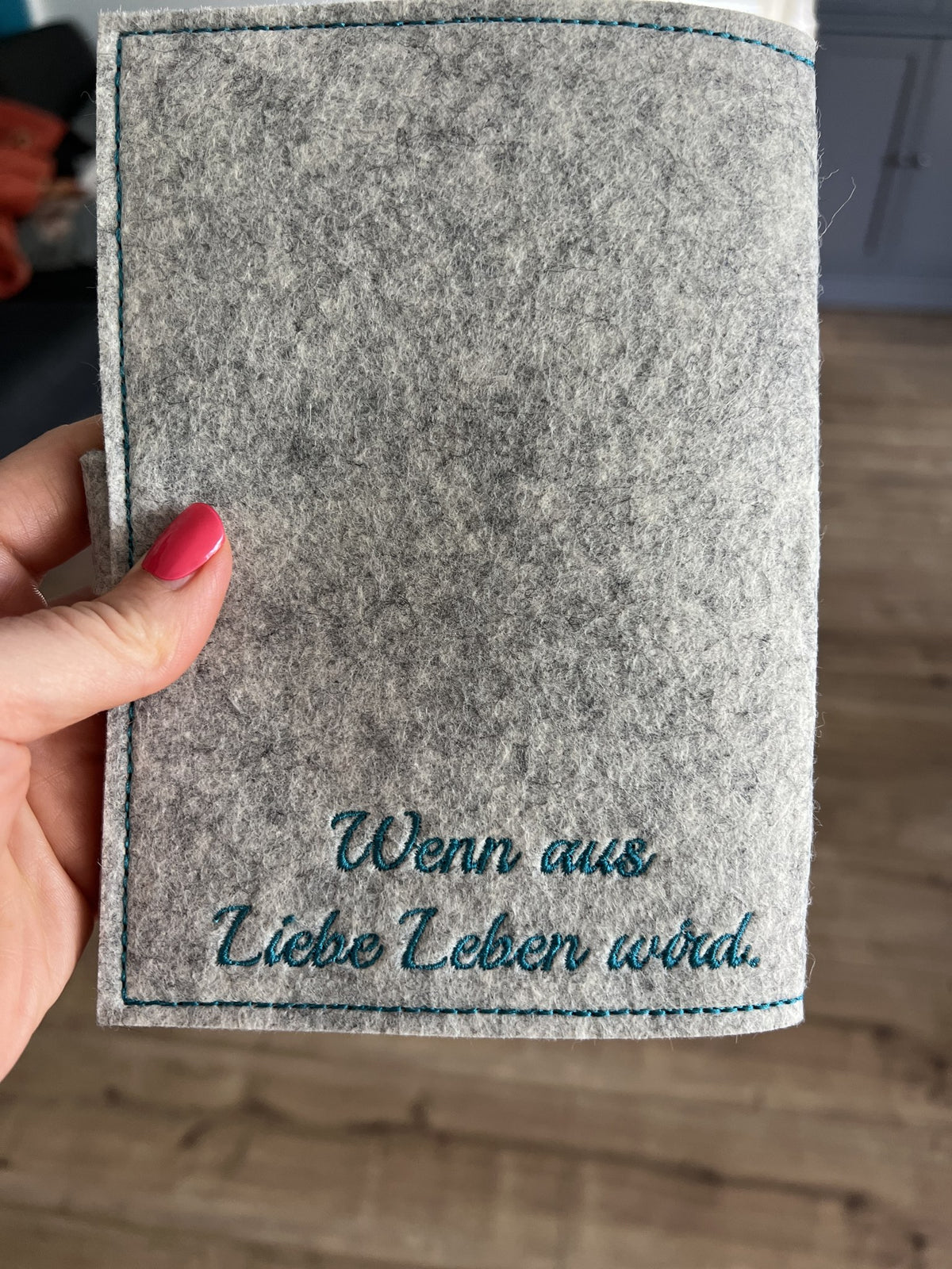 Rückseite einer grauen Mutterpasshülle mit gesticktem Spruch „Wenn aus Liebe Leben wird“